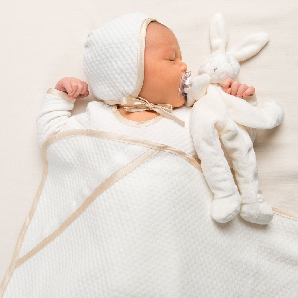 Photo of a newborn baby underneath the Liam Personalized Blanket. He is wearing the Quilted Newborn Romper and holding a stuffed animal bunny