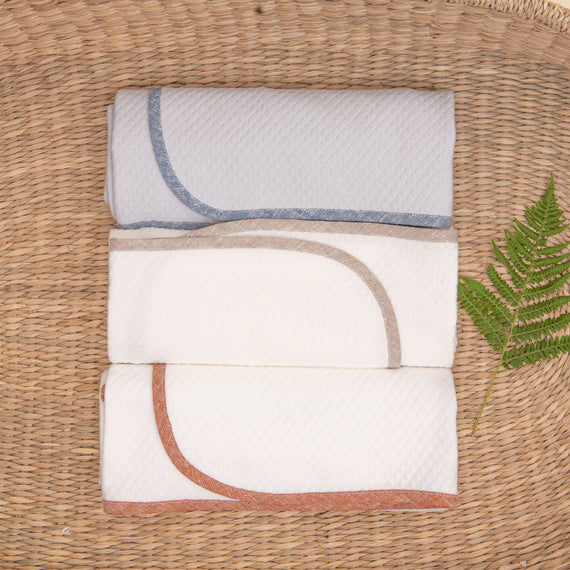 Photo of all three colors of the Silas Personalized Blanket in a woven basket. The three colors include clay, indigo, and sand