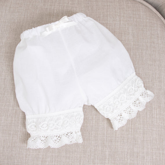 Isabella bloomers with lace trim for a christening, on a beige fabric background.