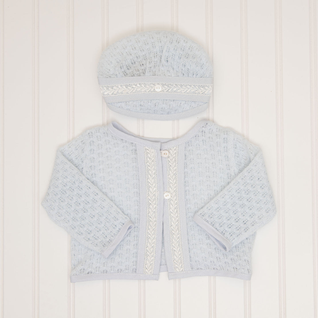 A flat lay of the Harrison Blue Knit Sweater and Blue Knit Hat, showcasing the fine lace trim and pearl-like buttons on the front.