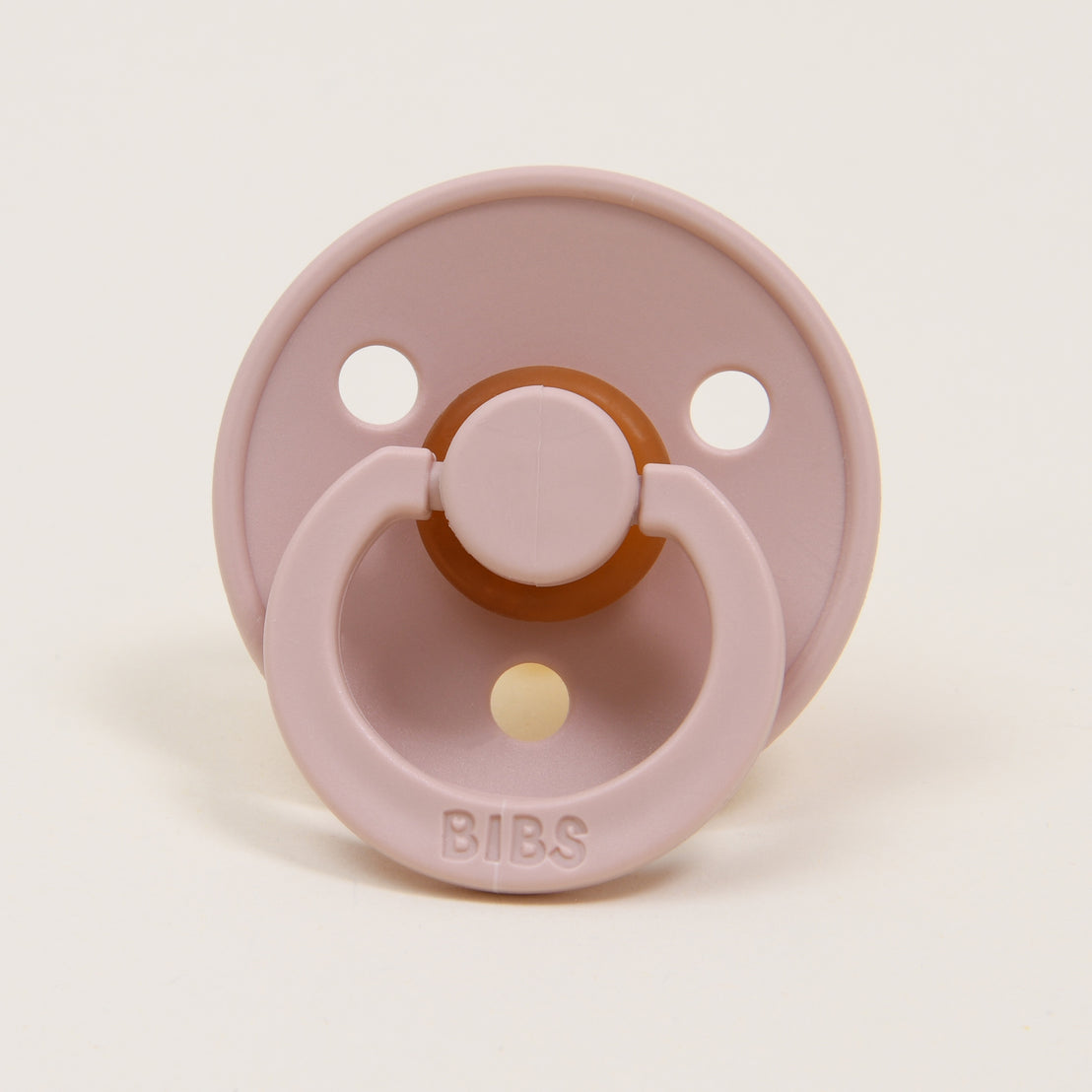 A Bibs Pacifier in Blush with a round shield and two ventilation holes, featuring a brown rubber nipple and a ring handle, set against a plain white background.