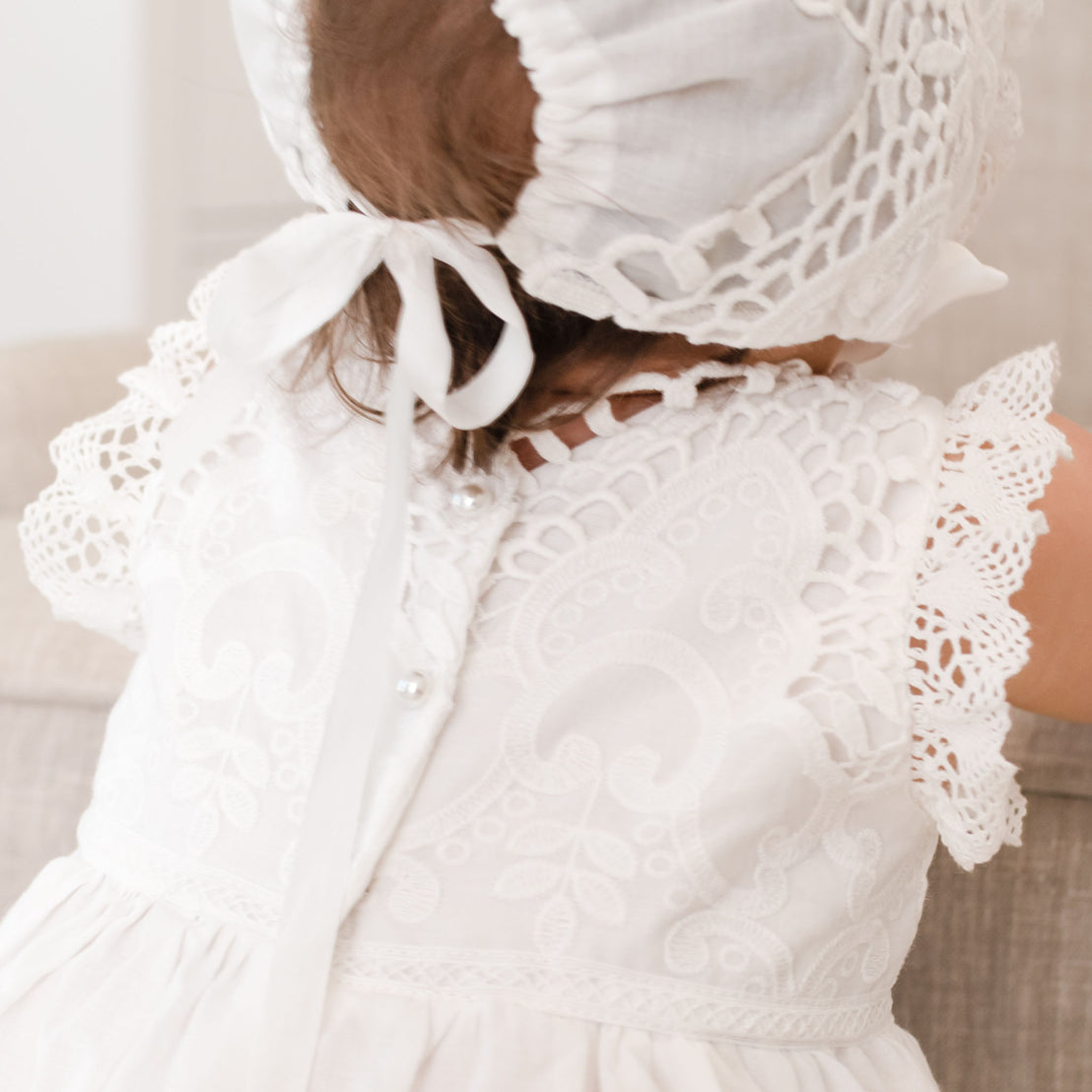 Back detail of the top bodice of a christening romper dress worn by a baby girl