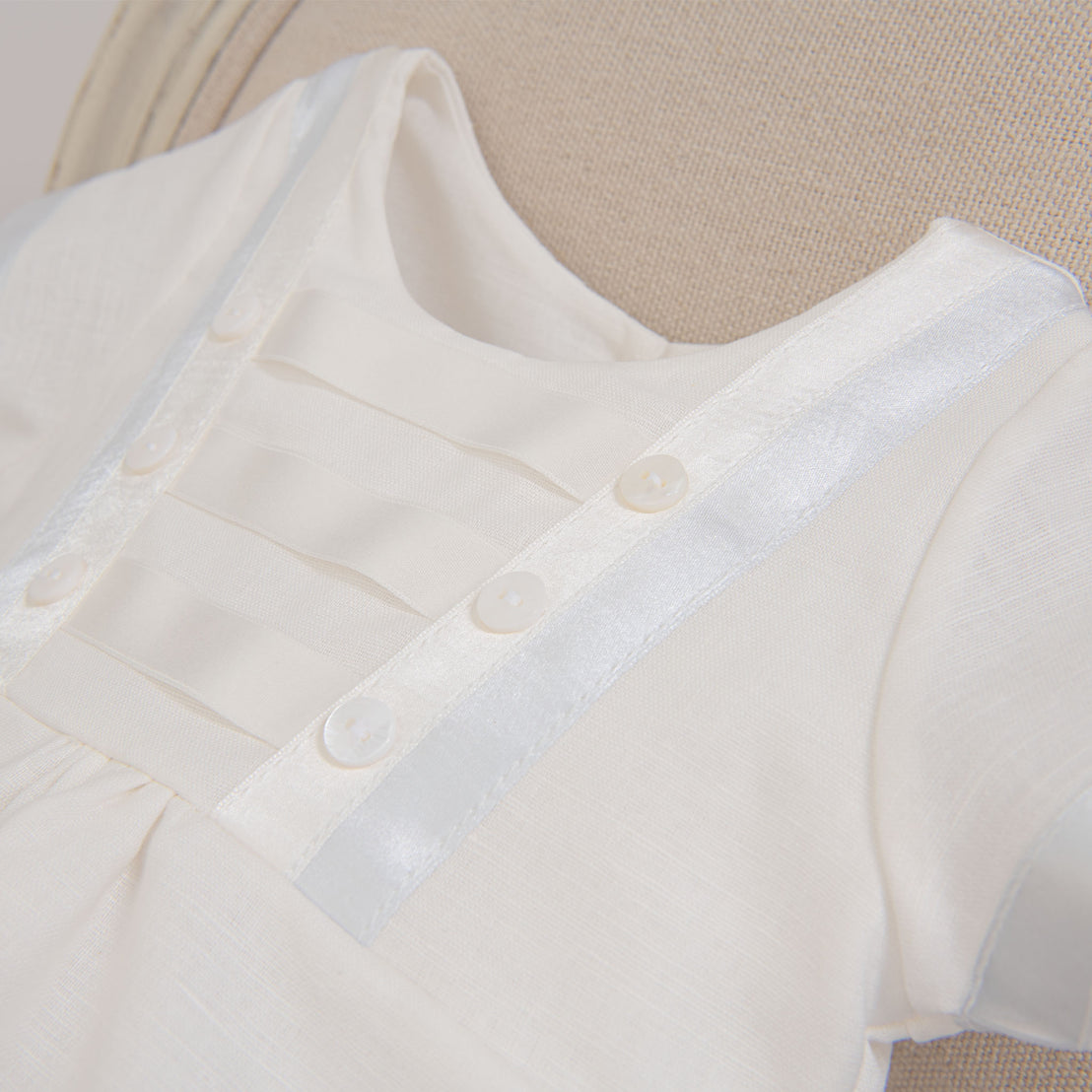 Flat lay photo showing the detail of the Owen Linen Romper with silk ribbon in ivory and light blue across the front