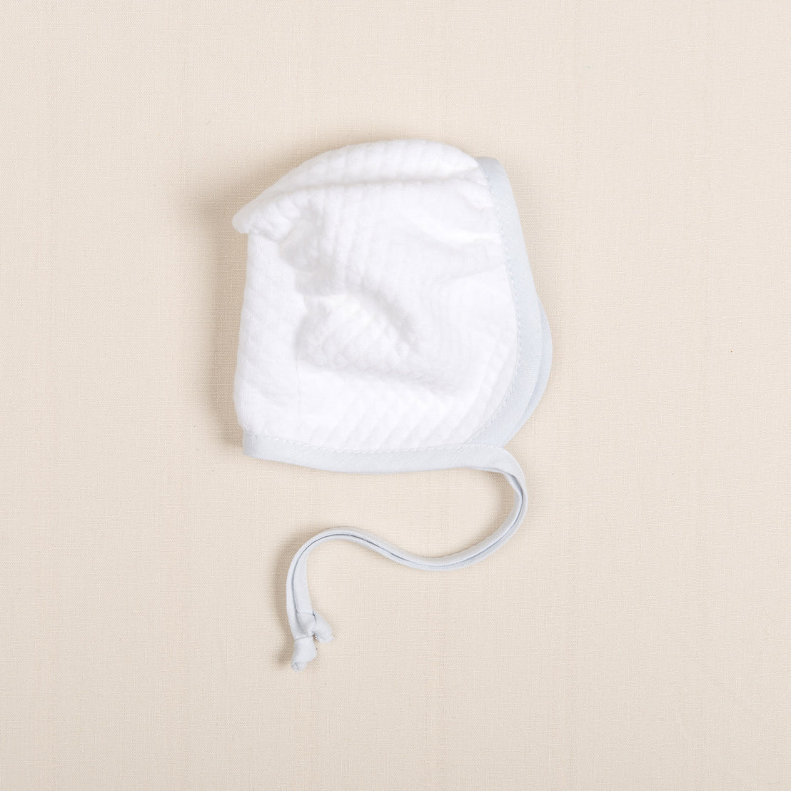 The Harrison quilted bonnet from the gift set, displayed flat to showcase its soft texture and delicate light blue trim.