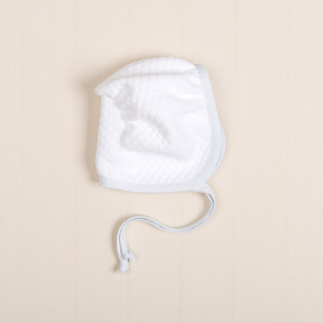 Flat lay photo of the Harrison Quilted Bonnet made with soft quilted cotton in white with a light blue trim linen. Blue linen ties allow for tying under the chin