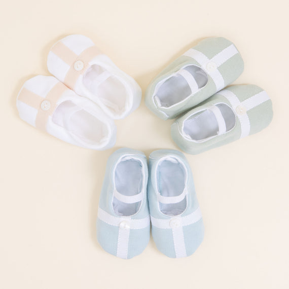 Flat lay photo showing the top detail of three pairs of Theodore Booties, including blue, green, and a white/tan color. The booties are made from a 100% French Terry Cotton with a Grosgrain Trim (with button detail) and soft elastic strap.