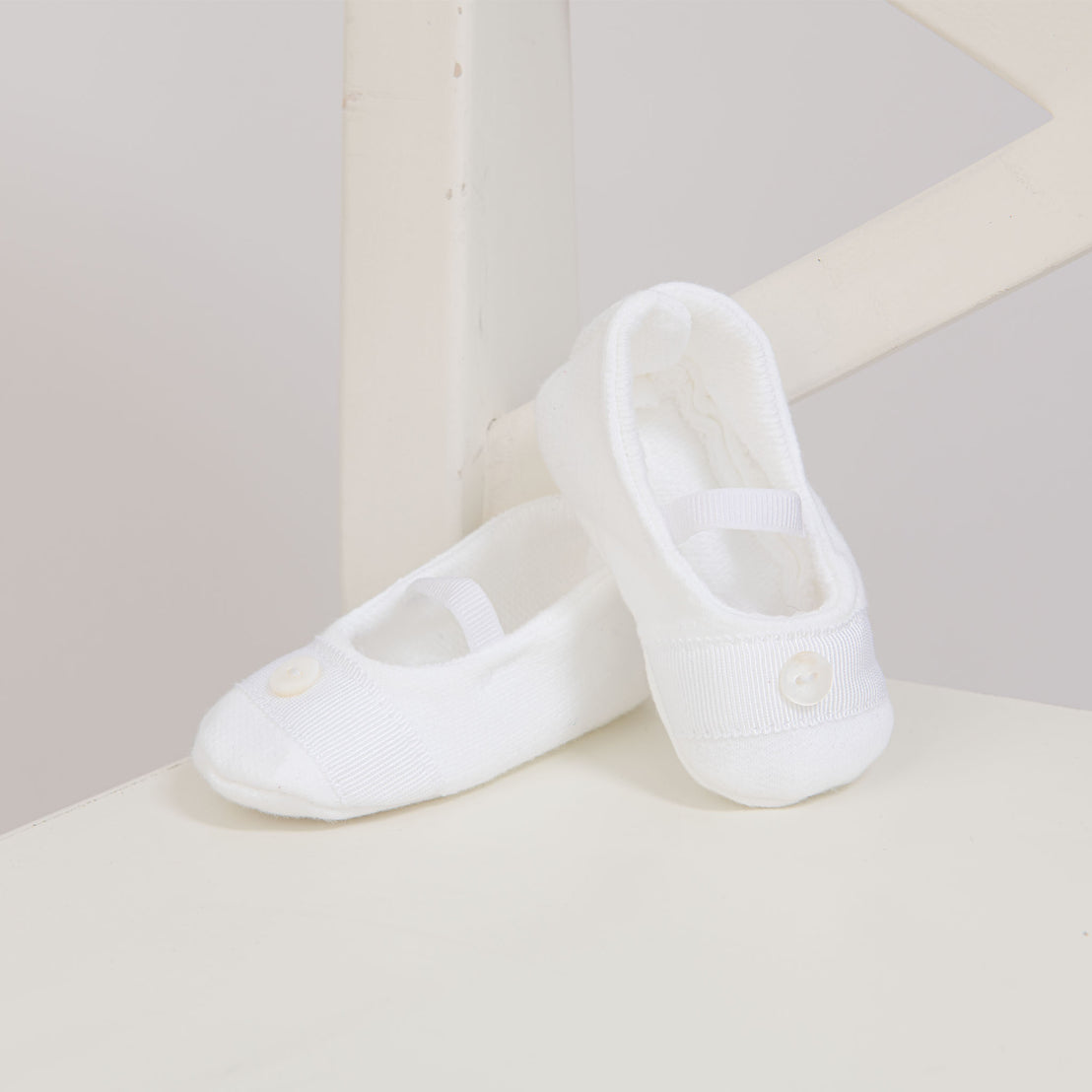 Flat lay photo of a pair of Elliott Booties made from white French terry and featuring grosgrain ribbon detailing across the toe with a button. 