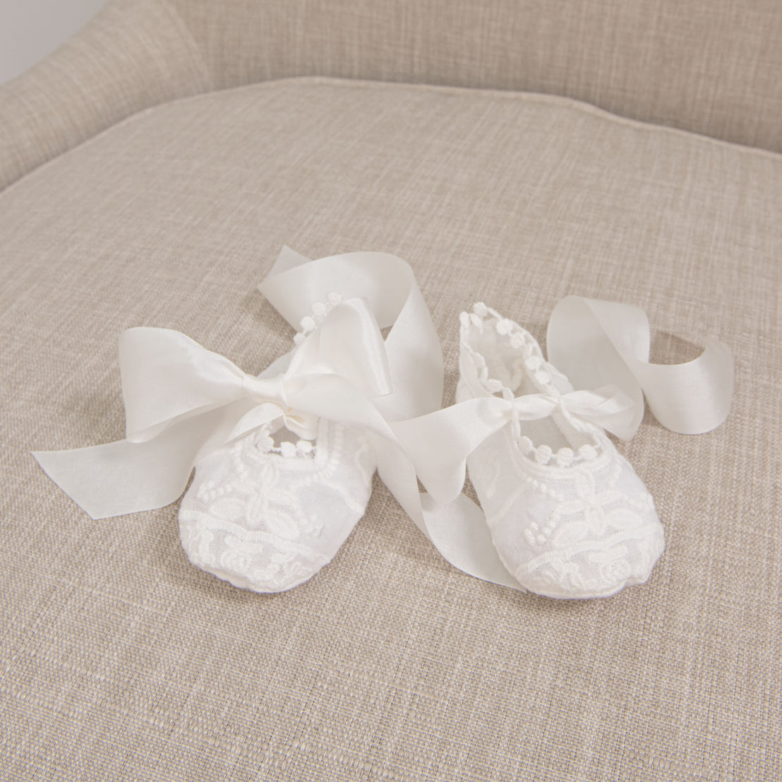 Flat lay of Lily Booties showing the details of the soft cotton lace in light ivory with silk ribbon ties