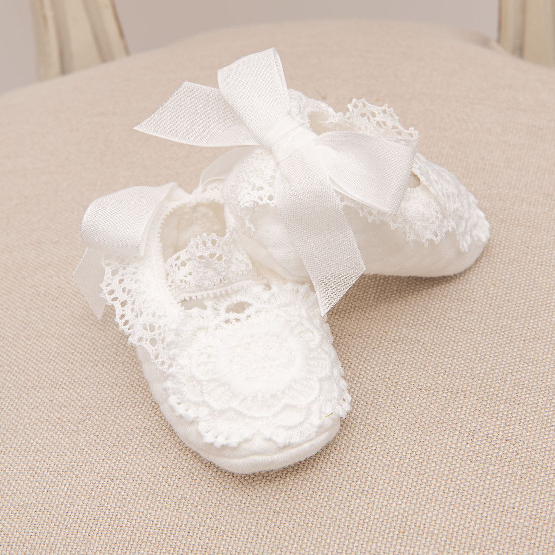 Close up photograph of the Poppy baby girl booties on a chair. Made with cotton and beautiful lace.