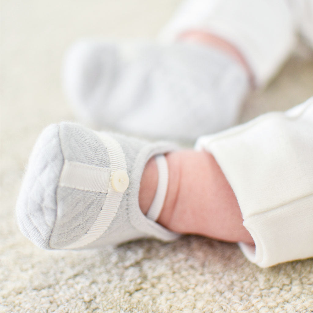 Photo of baby wearing the Grayson trim quilted booties with satin trim. 