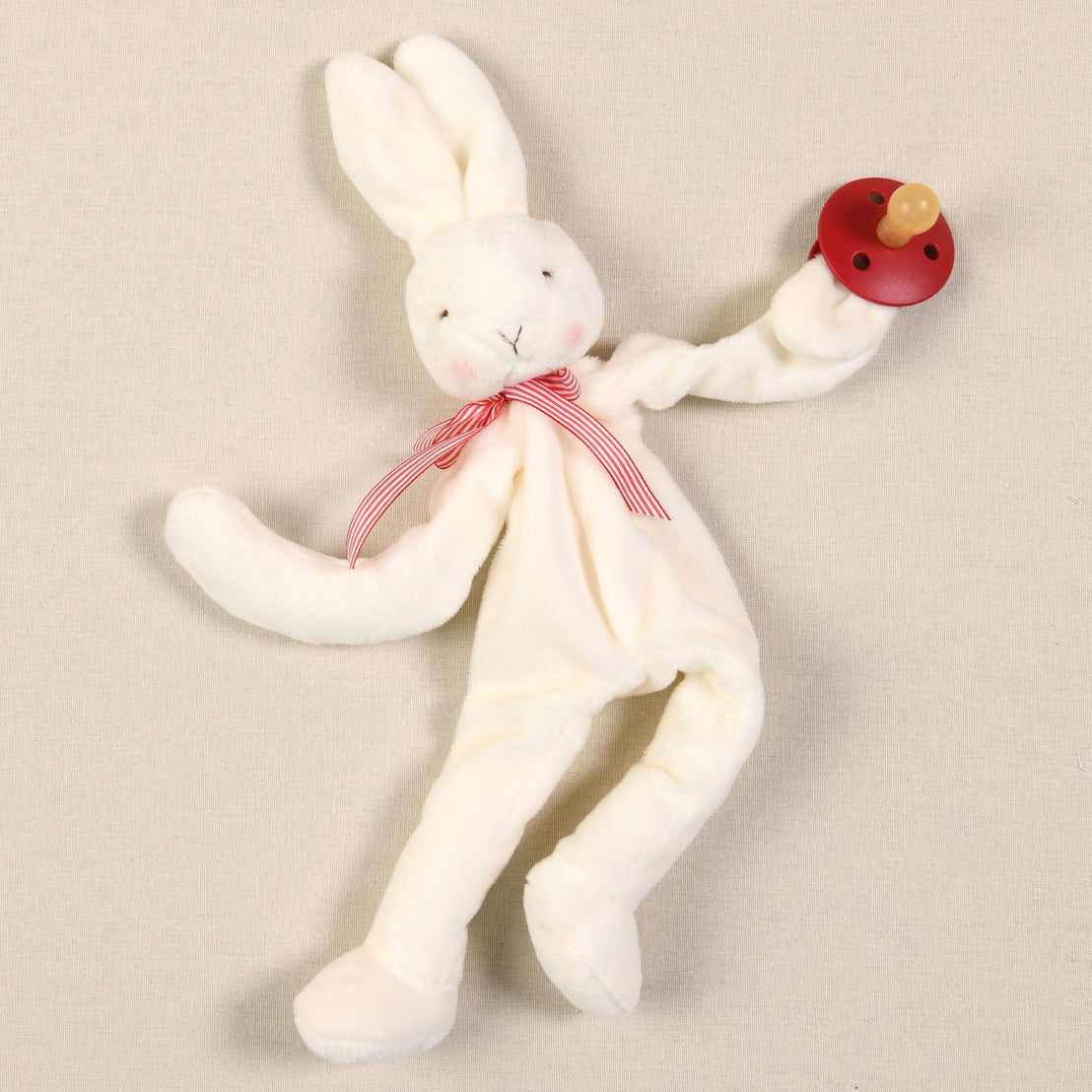 The Silly Bunny Buddy & Pacifier, featuring a plush velour bunny adorned with a red and white striped ribbon around its neck, cradles a wooden toy rattle, making it the perfect baby gift. With long ears and an elegantly embroidered face, this delightful bunny sits on a beige background, ready to become your baby's cherished pacifier holder companion.