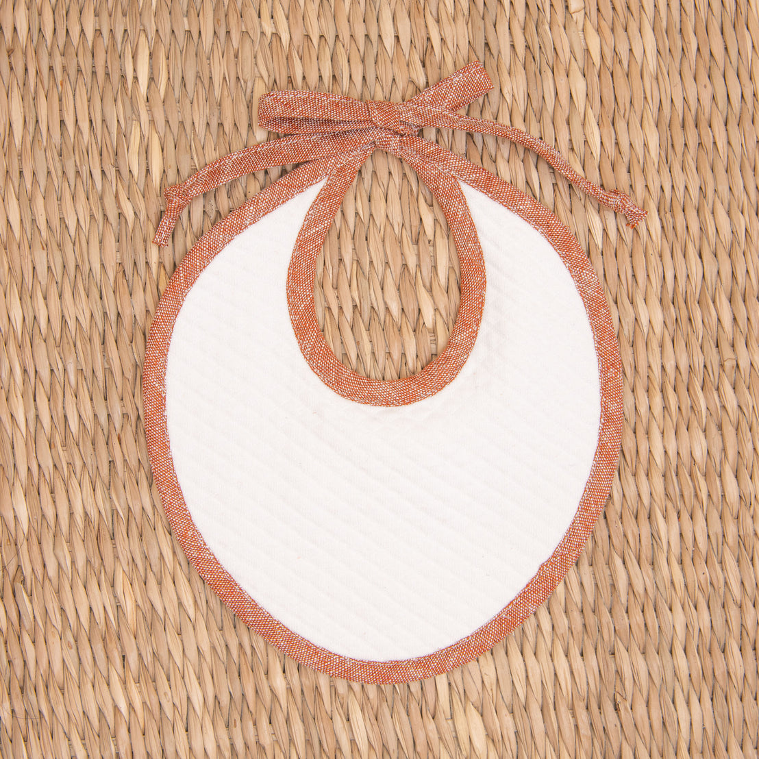 Flat lay photo of the red Silas Linen Trim Bib. The bib is made from textured cotton in light ivory