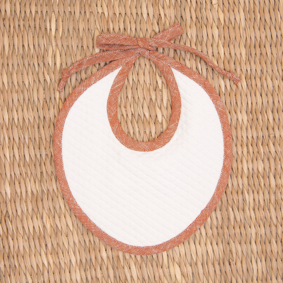 Flat lay photo of the red Silas Linen Trim Bib. The bib is made from textured cotton in light ivory