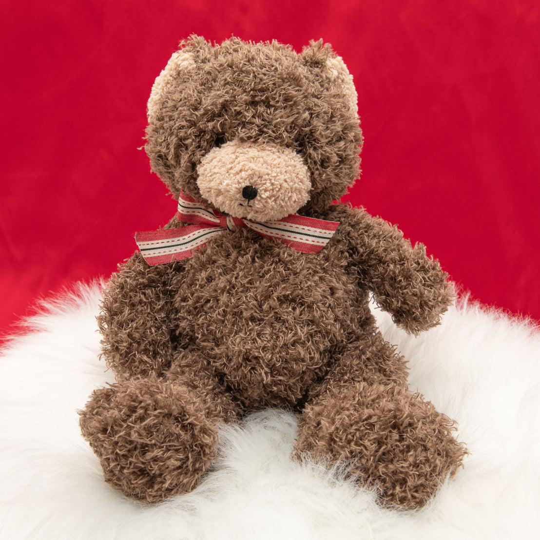 A photo of the Cubby Bear, a soft stuffed animal bear, sitting on a white fur rug.