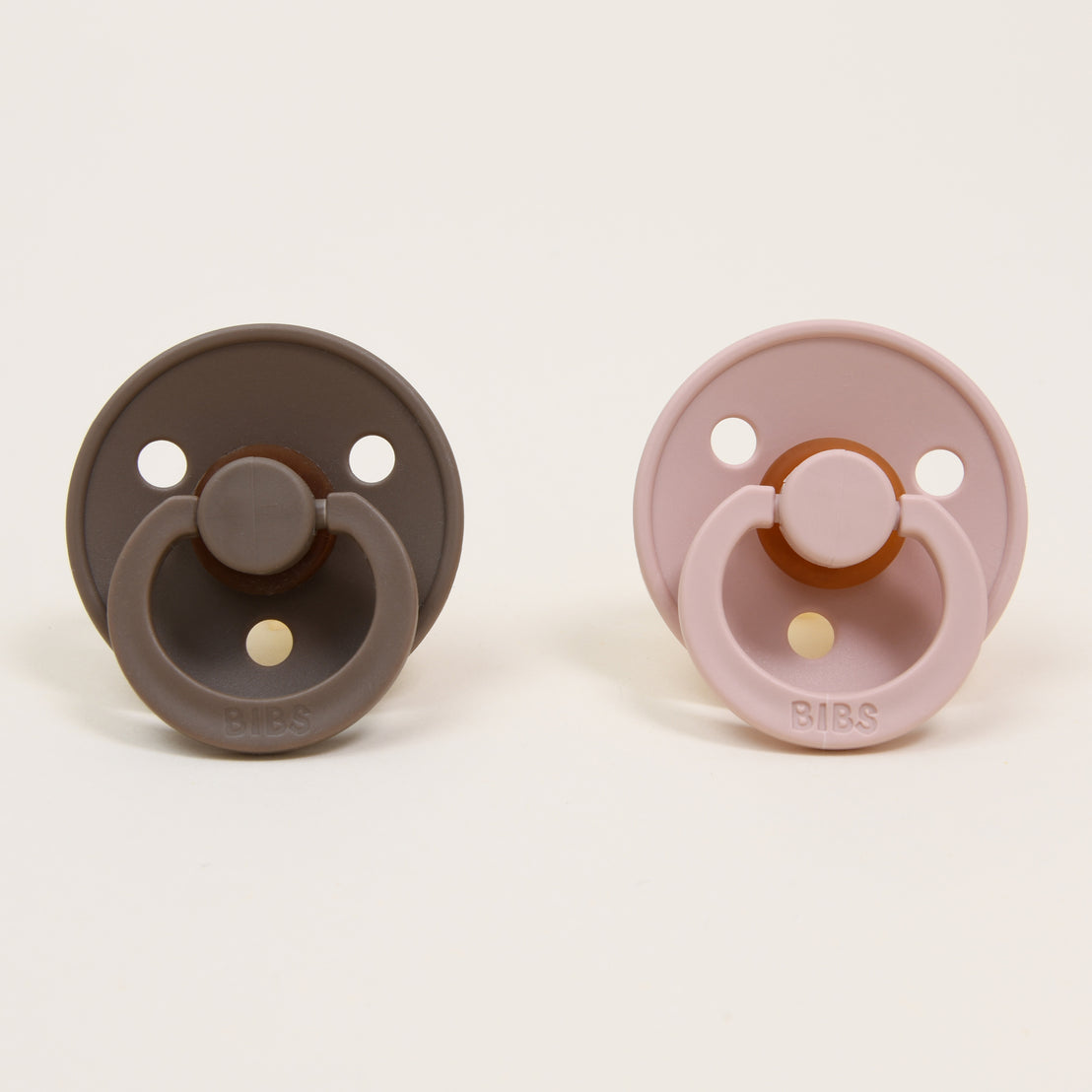 Two Bibs Pacifiers, one brown and one pink, displayed against a plain white background.