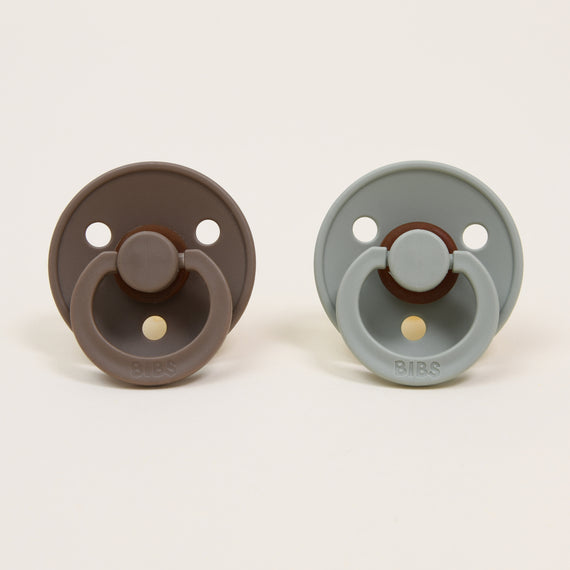 Two Bibs Pacifiers in "dark oak" and "sage" colors against a plain background.