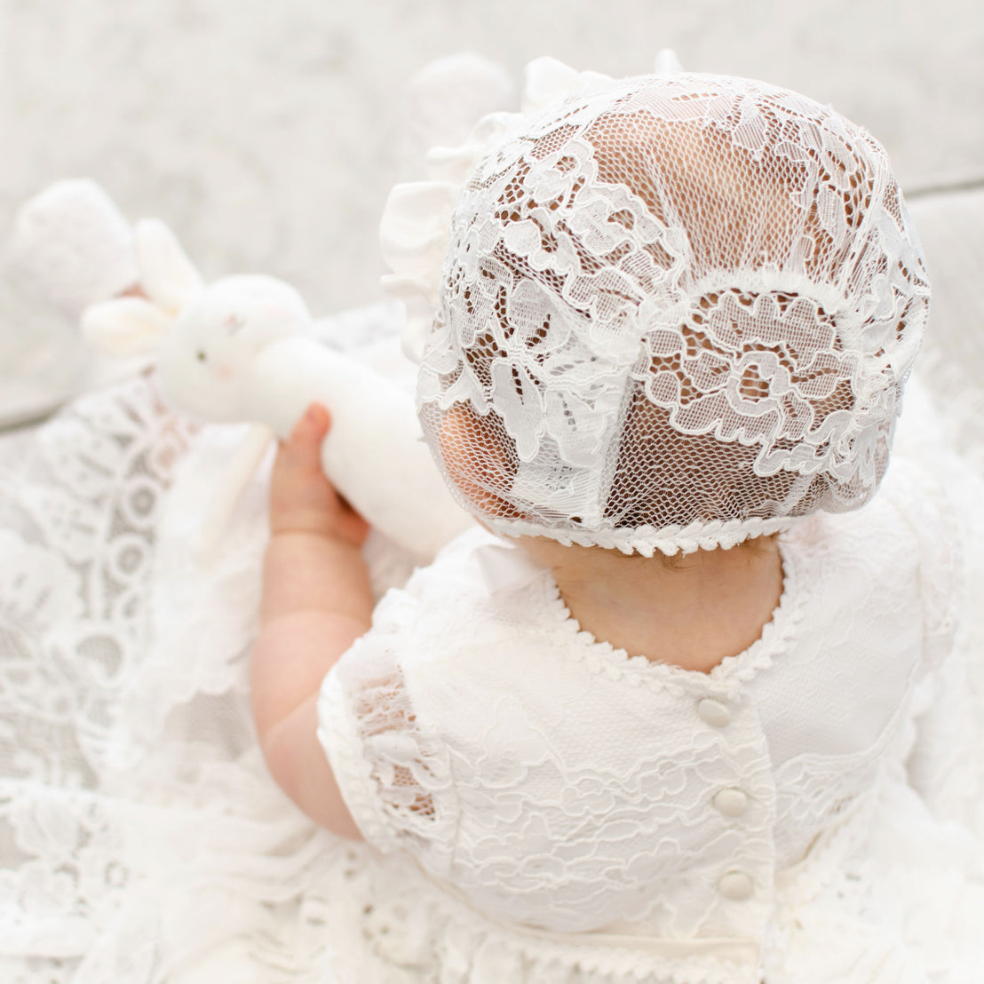 The back of a baby's head wearing the Victoria Lace Christening Bonnet. 