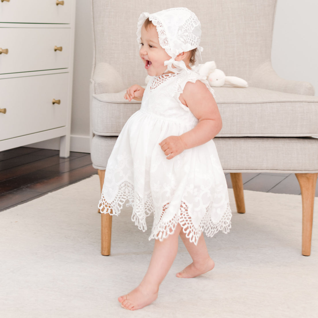 Baby walking and smiling as she wears a christening romper dress