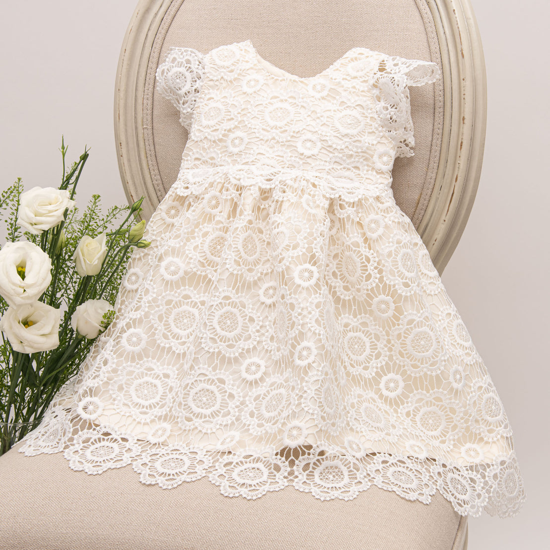 Product photo of the poppy cotton lace fancy baby dress on top of a chair. 