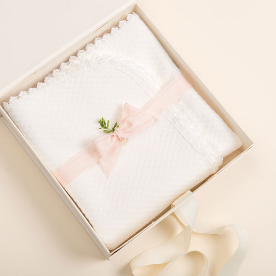 An elegant Baby Beau & Belle gift box with a magnetic closure containing a delicate white lace handkerchief adorned with a pink ribbon and a small green and white floral embellishment, presented on a soft cream background.