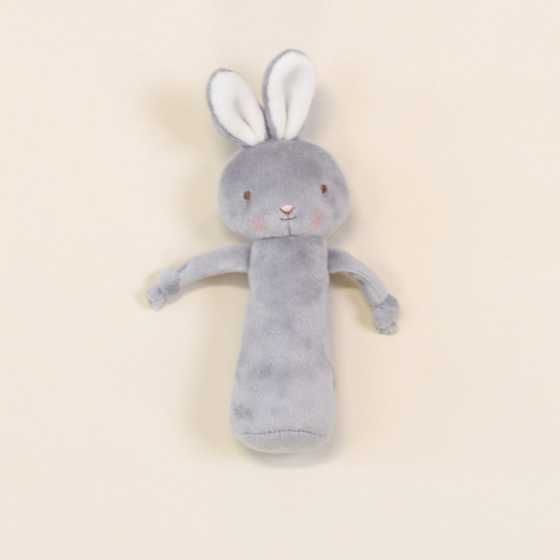 A soft and baby-safe Friendly Chime Rattle in gray, featuring velour chimes and long ears, is set against a light beige background. This plush toy boasts pink cheeks and a cylindrical body with delicately embroidered facial features, making it ideal for gentle play.