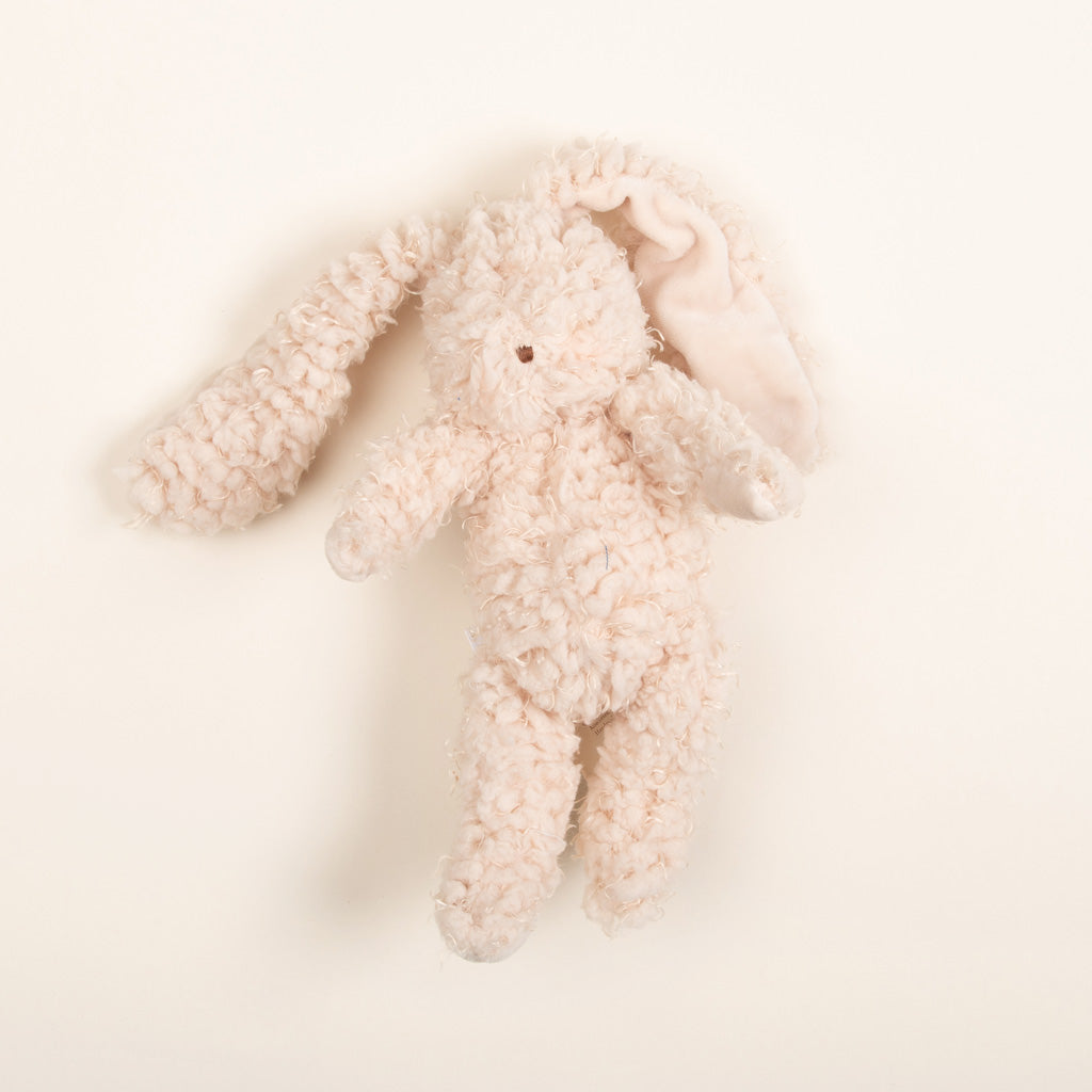 Flat lay photo of a super soft bunny stuffed animal made with warm almond scraggly fur body with embroidered face