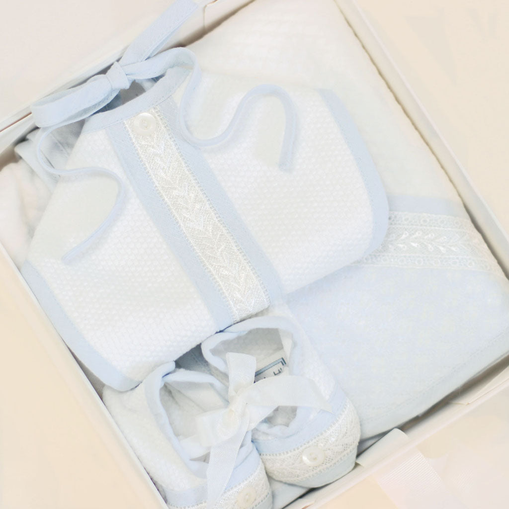 A Baby Beau & Belle gift box with a magnetic closure containing baby items: a light blue bib, a white blanket with lace trim, and matching baby booties, all neatly arranged in small gift wrap with a bow.