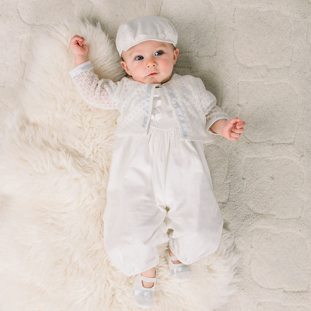 Baby boy laying on the ground and wearing the Owen Knit Sweater, matching romper and newsboy cap