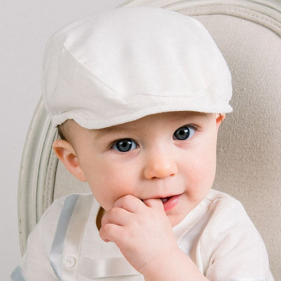 Baby boy wearing a Oliver Linen Newsboy Cap in white. It is made linen cotton blend and features a soft elastic band around the back.