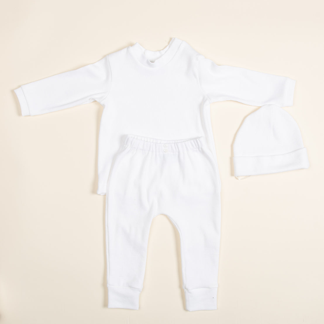 Introducing the Ivory Pima Top & Leggings set, a handcrafted baby outfit from the USA. This ensemble, featuring a long-sleeved top, matching leggings, and a cozy hat is crafted from soft Pima cotton. Arranged on a light background, it presents a simple yet elegant minimalist design.