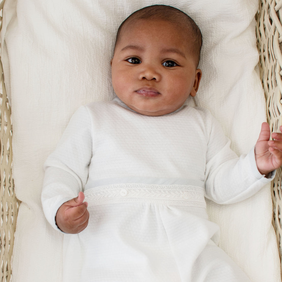 A baby laying in a crib and wearing the Harrison Long Sleeve Romper made from textured white cotton