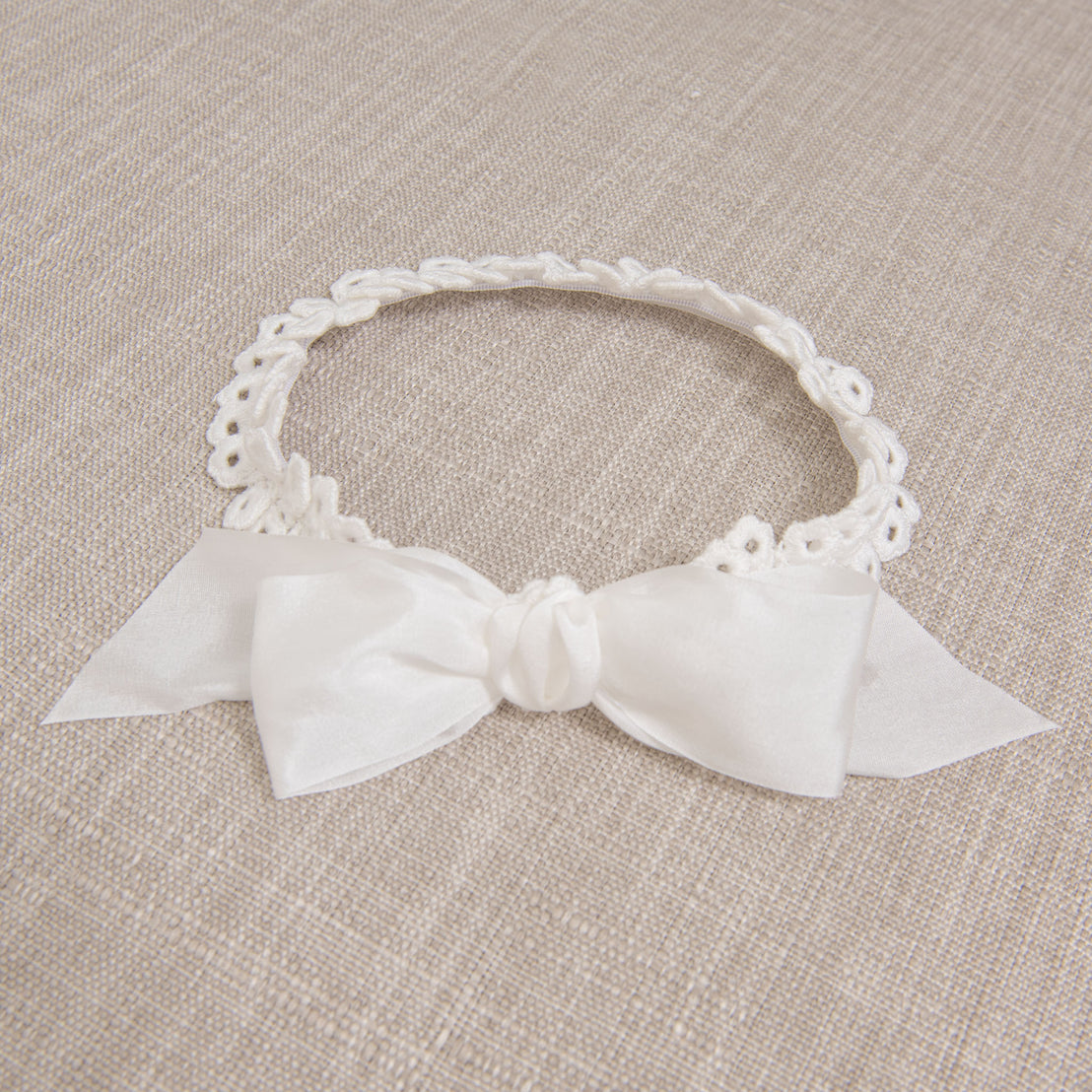 Flat lay photo showing the details of the Lily Bow Headband, including the soft, cotton lace in Light Ivory with elastic and the silk ribbon bow
