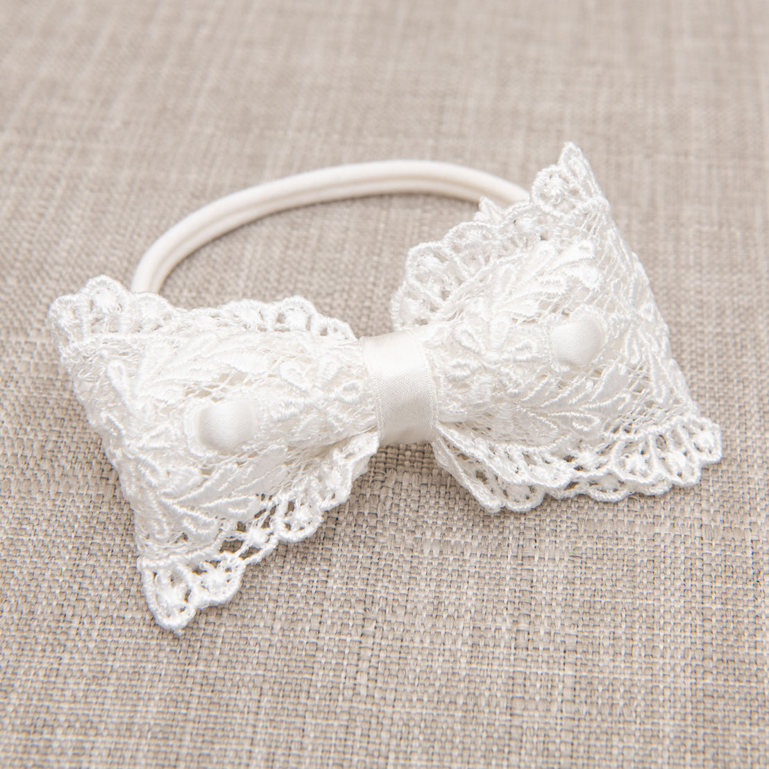 An upscale Madeline Lace Bow Headband, displayed against a textured beige fabric background.