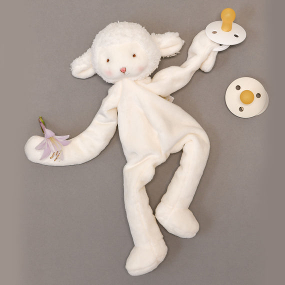 A vintage Silly Lamb Buddy plush comfort toy laying flat with a pacifier and a small white flower beside it on a gray background.