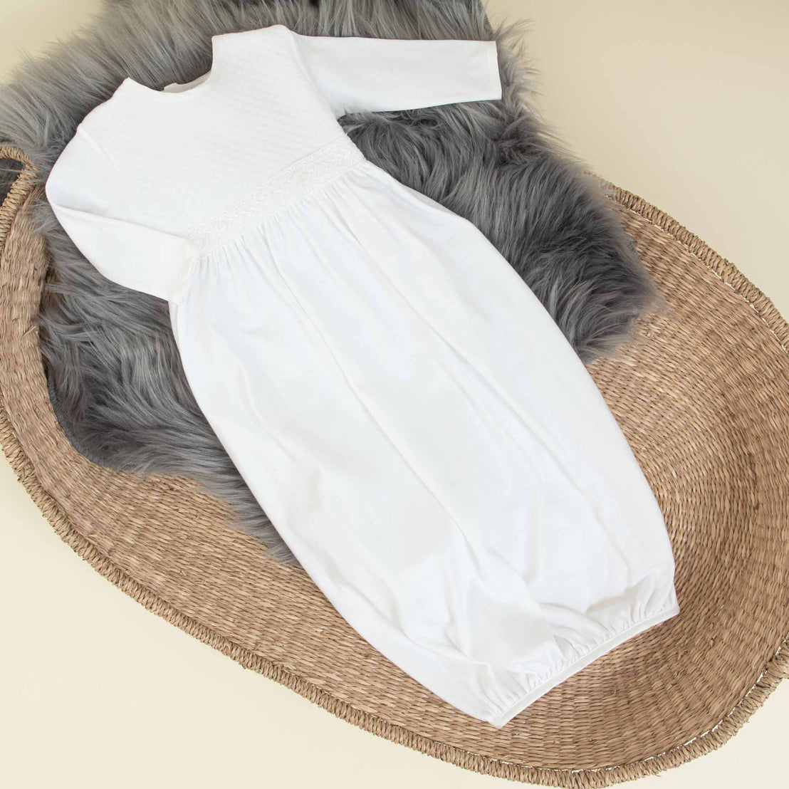 Flat lay photo the Elijah Newborn Gown in a cradle with a grey fur blanket