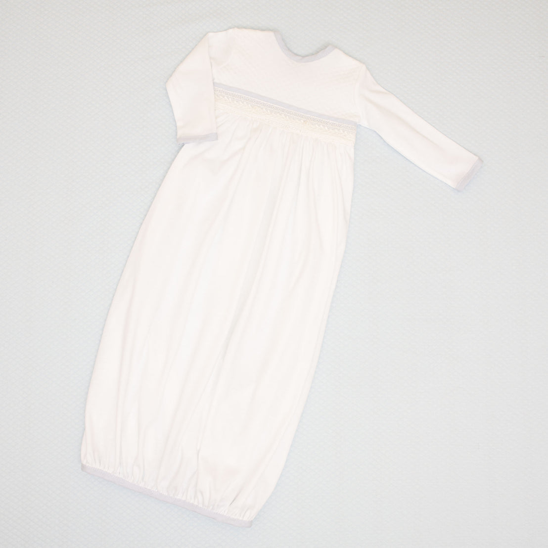 Flat lay photo of the Harrison Newborn Gown made with soft pima cotton in white and features a plush white quilt bodice. Along the waist is an ivory Venice lace accent and features an open skirt design