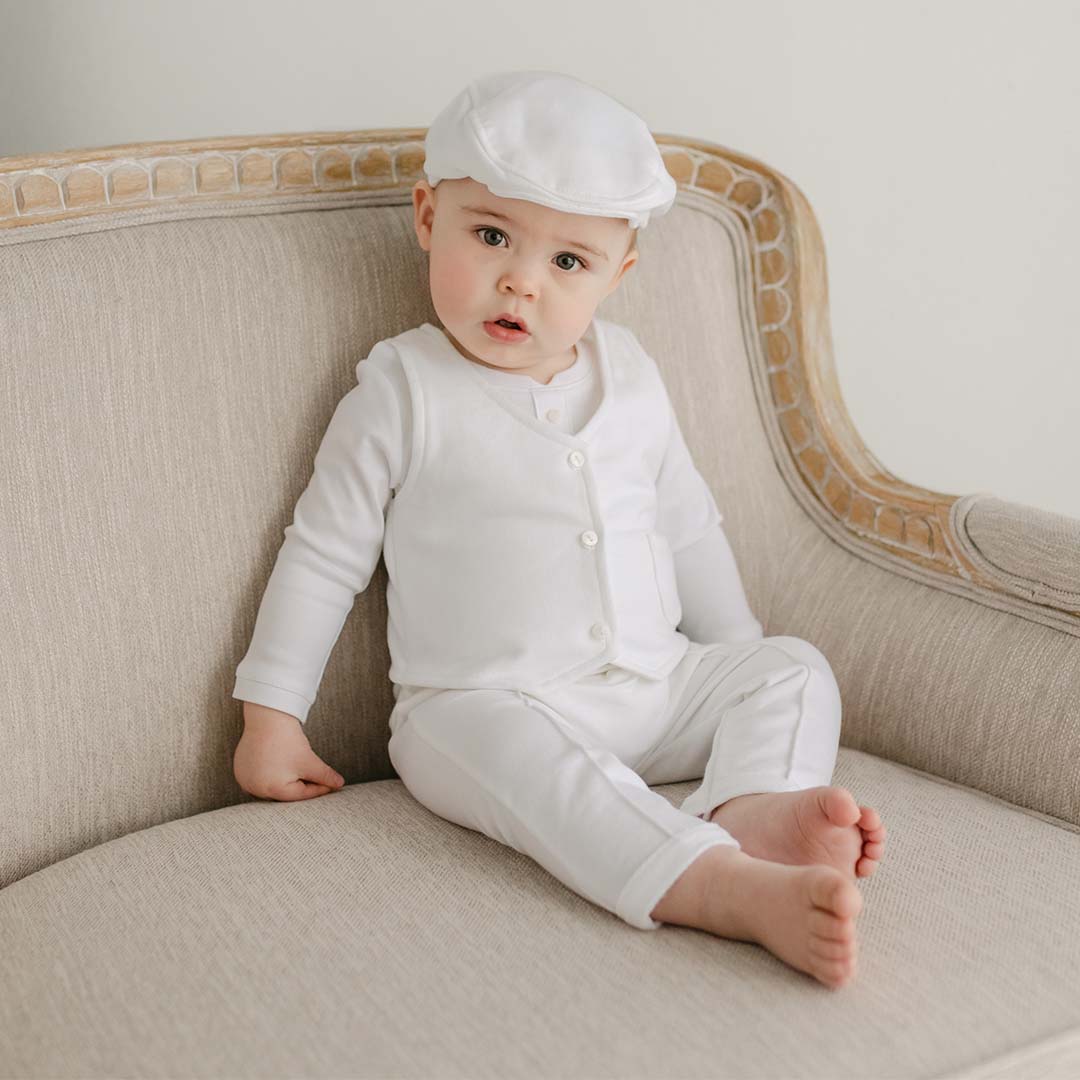 Baby boy sitting on a chair wearing the Miles vest Suit and Newsboy Cap made with french terry in white