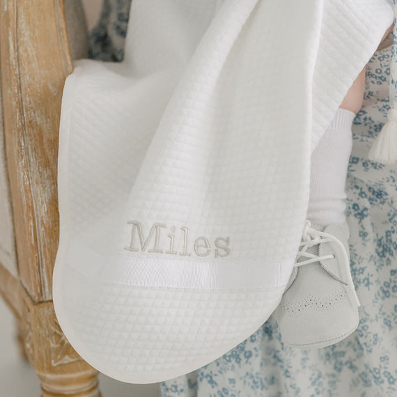 Photo of the Miles Personalized Blanket. It is made with quilted cotton and a ribbon detail on the corner. The name "Miles" is embroidered on the corner.