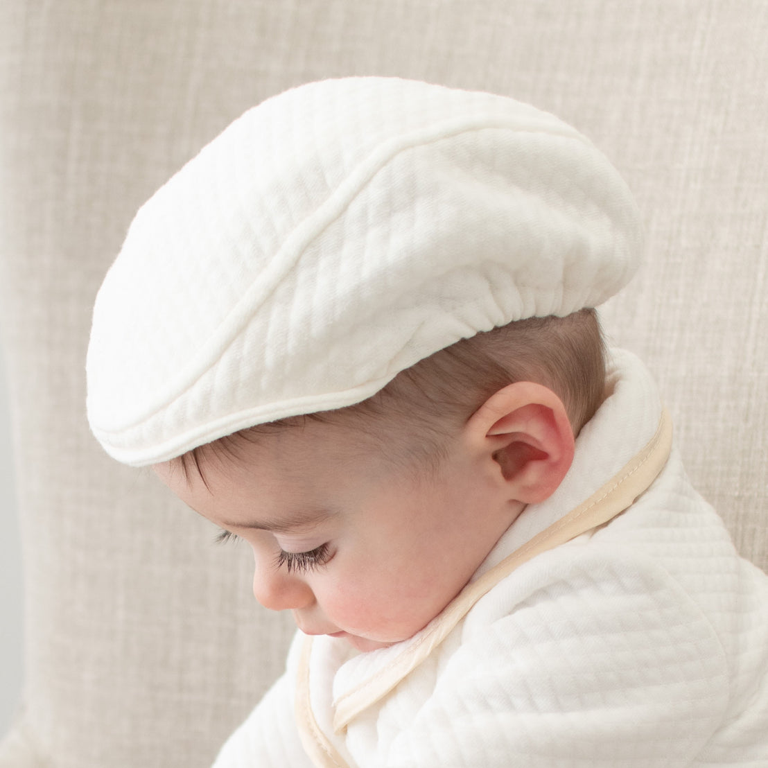 Baby boy sitting on a chair. He is wearing the Liam Newsboy Cap made of white quilt