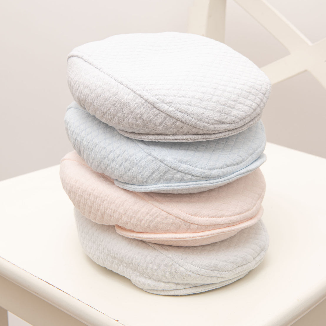 Flat lay photo of the four Asher Quilted Newsboy Caps in colors grey, pink, powder blue and soft teal.