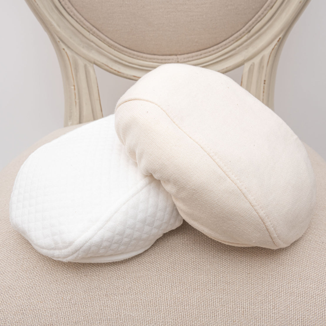Flat lay photo of both types of Braden Newsboy Caps, including the white quilt and ivory french terry