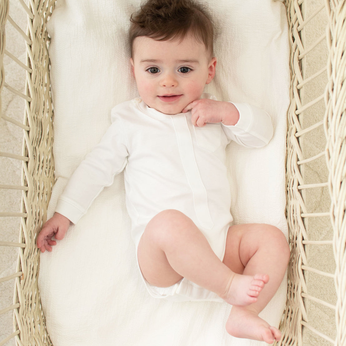 A baby sits in a cradle and is wearing a white onesie