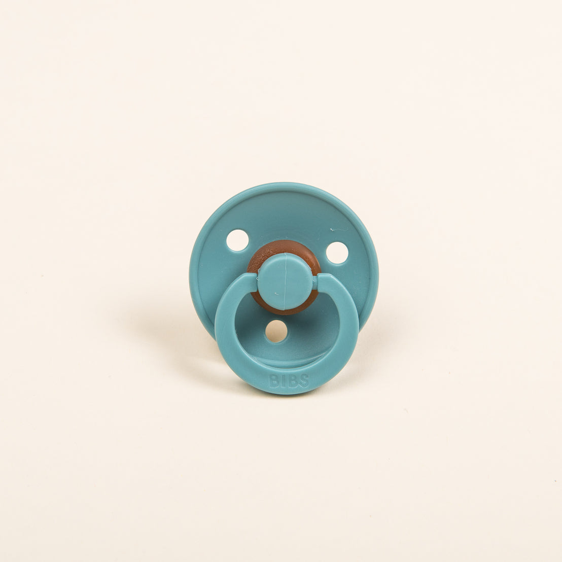 Aiden Silly Bunny Buddy & Pacifier: A teal-colored baby pacifier with a round shield and a wooden pull knob, perfect for coming home from the hospital, placed against a plain light beige background.