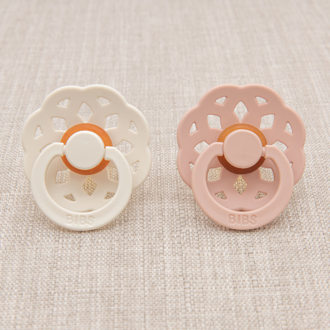 Two bibs baby pacifiers - one in ivory and one in blush.