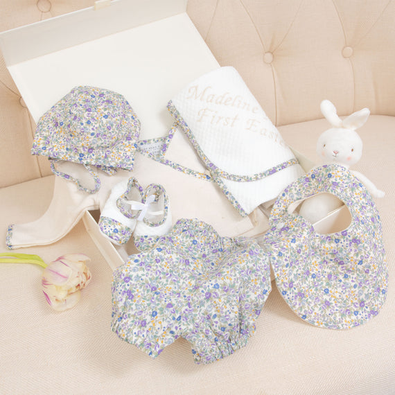 A boutique collection of Petite Fleur Gift Sets - Save 10% including a floral hat, shoes, and bibs, and a vintage-inspired plush bunny, displayed on a cream sofa with a tulip nearby.
