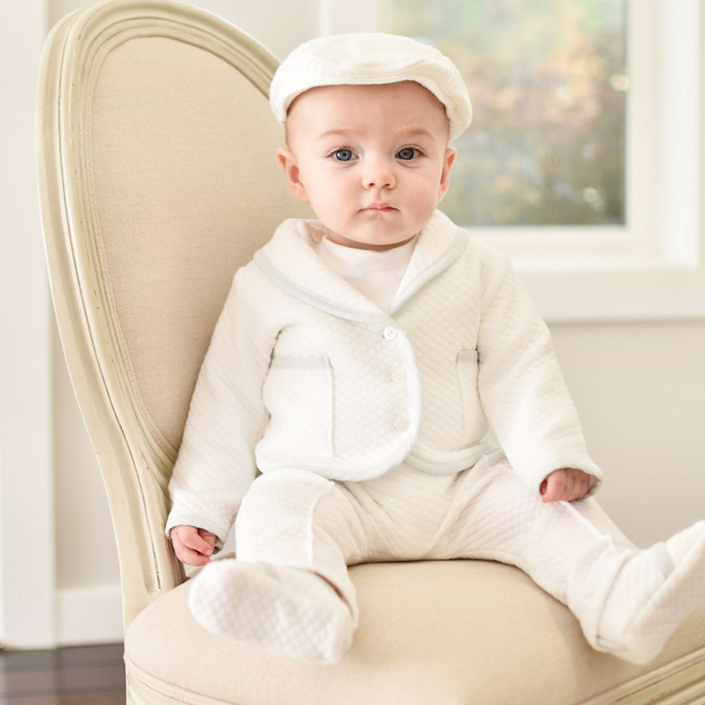 Baby boy sitting on a chair wearing the Harrison 3-Piece Pants Suit made with plush white quilted cotton jack, pants, hat, and booties