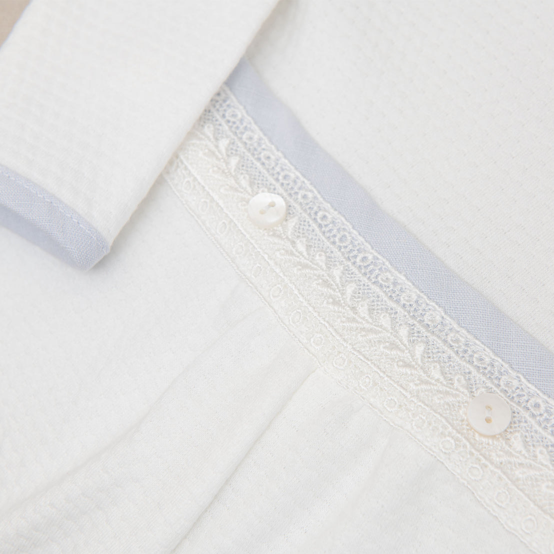 Close-up of the Harrison Long Sleeve Romper waistband, highlighting its lace embroidery, buttons, and soft blue trim.