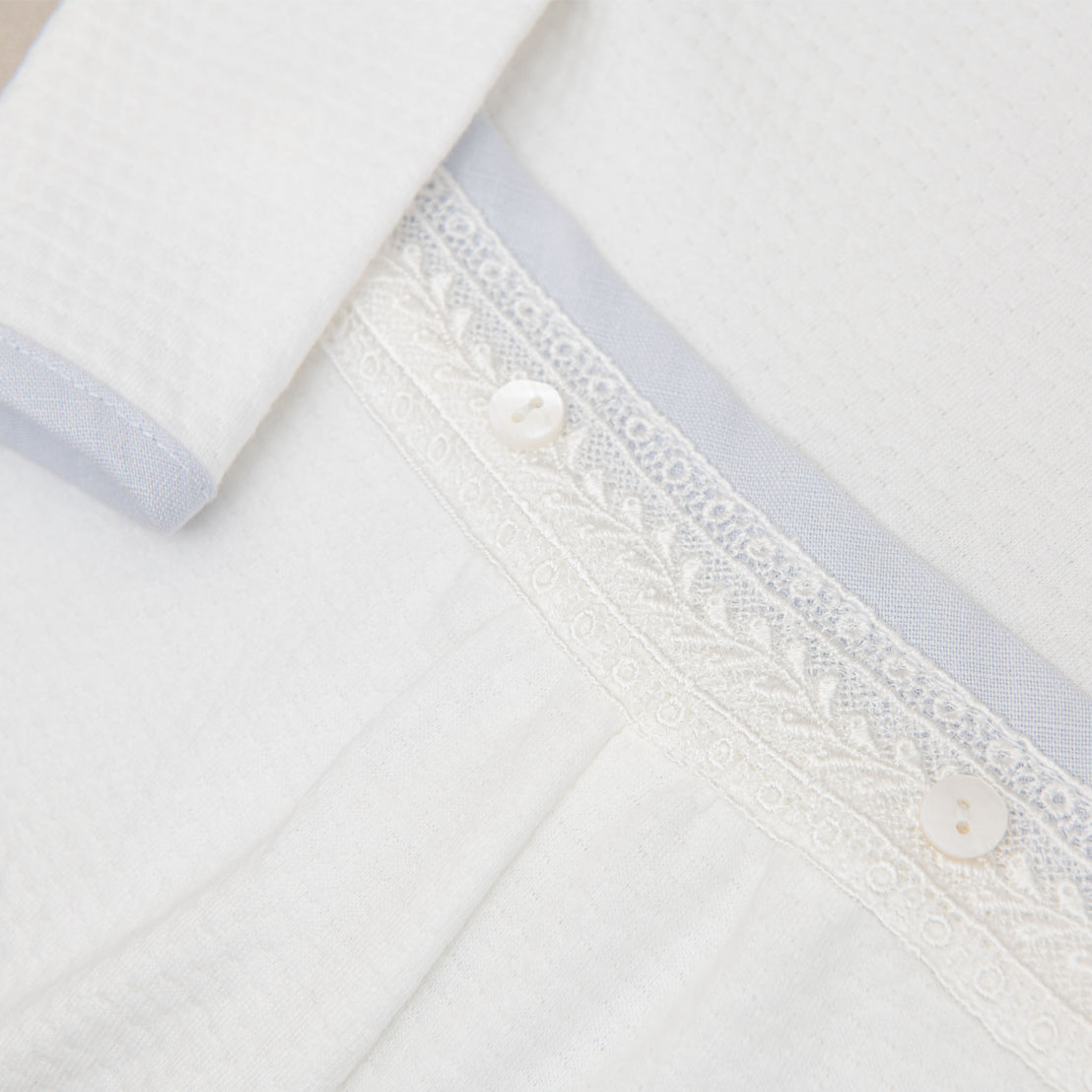 Close up detail of the Harrison Long Sleeve Romper featuring ivory Venice Lace and a blue cotton/linen edging