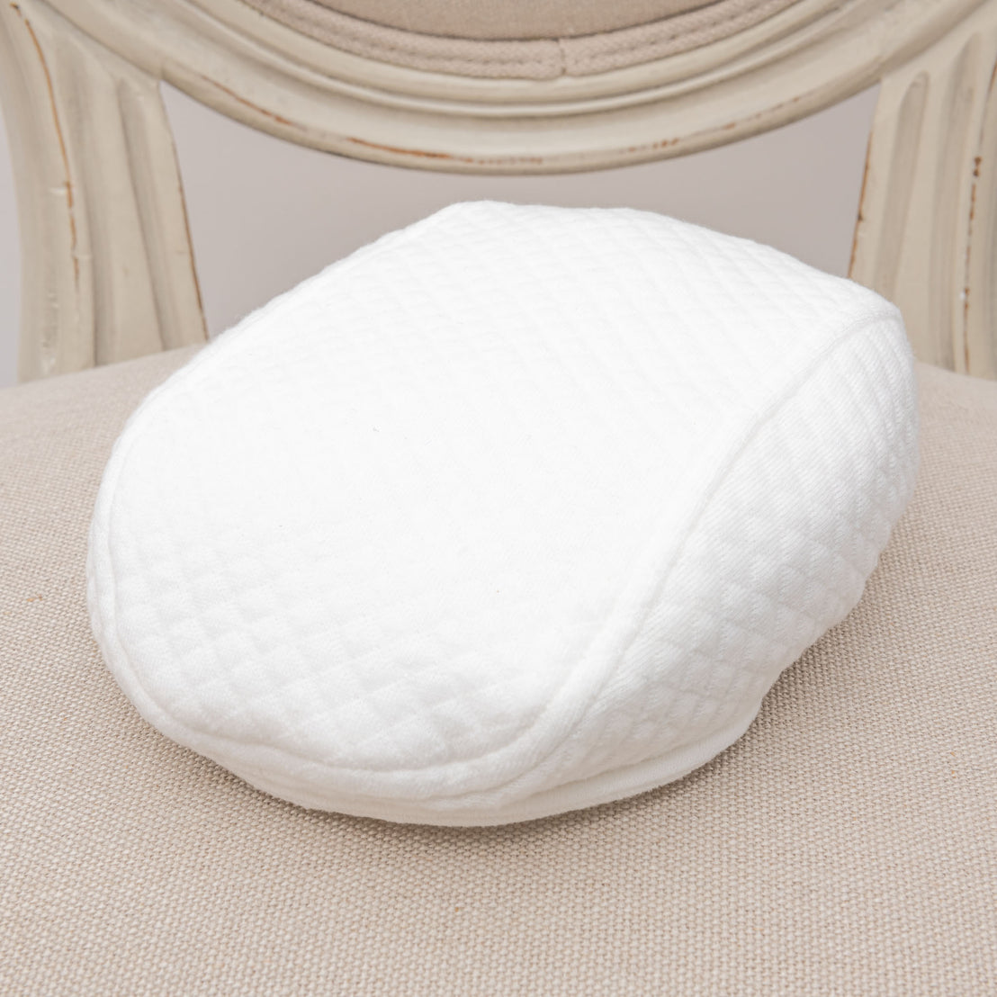 Flat lay photo of the white quilt Braden Newsboy Cap on a chair