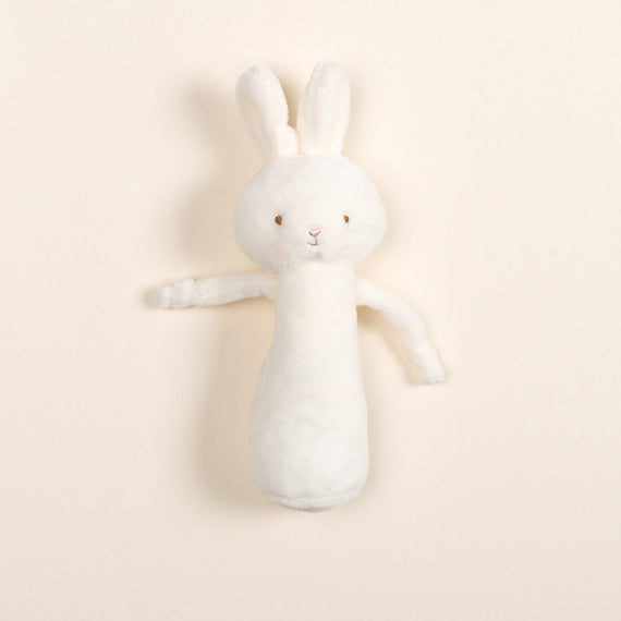 Introducing the White Bunny Chime Rattle: a sweet companion crafted from baby-safe materials, this plush toy rabbit showcases floppy ears and a simple embroidered face. Its soft, elongated white velour body rests elegantly against a light beige backdrop, capturing a nostalgic charm.